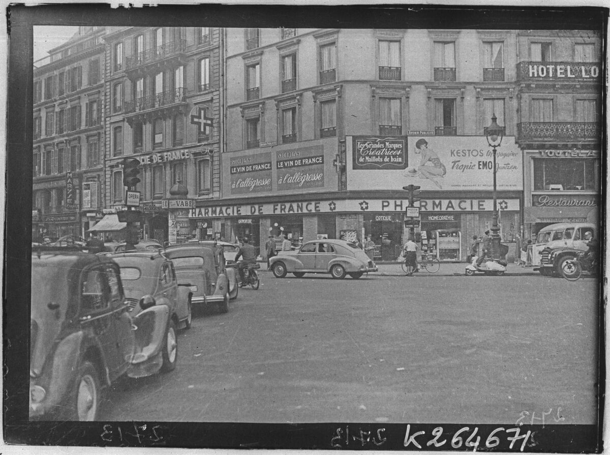 Vue de rue avec panneaux publicitaires et circulation à Paris vers 1950